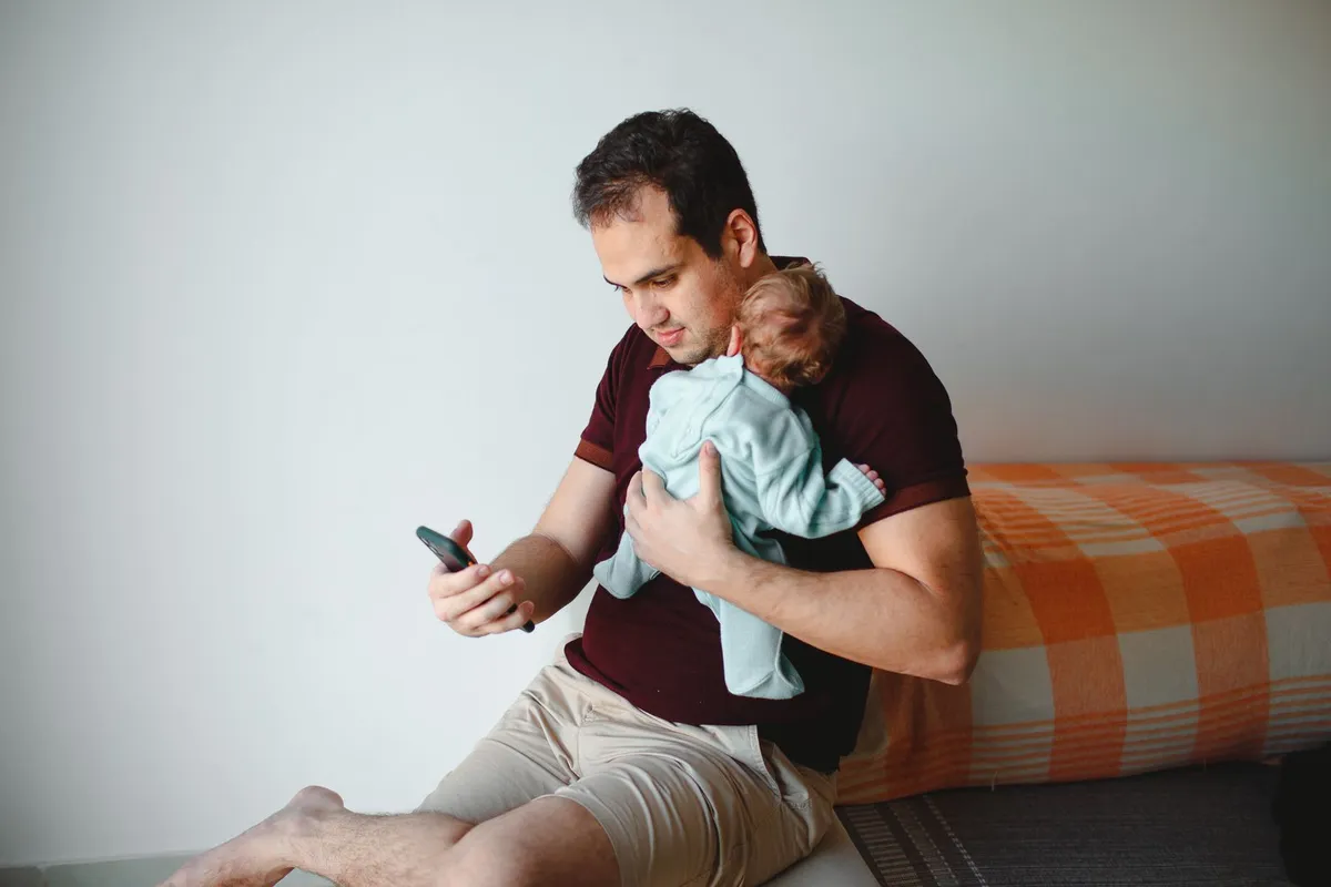 Vader met baby op de arm kijkt op zijn smartphone