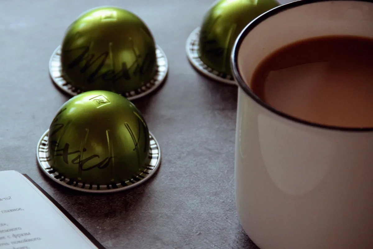 Groene Vertuo-koffiecapsules naast een mok koffie op een grijze tafel