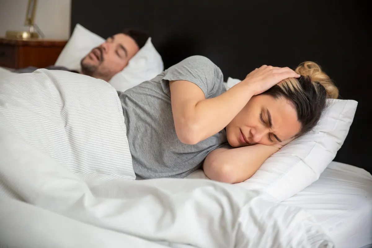 Vrouw houdt haar handen tegen haar oren terwijl haar partner naast haar snurkt