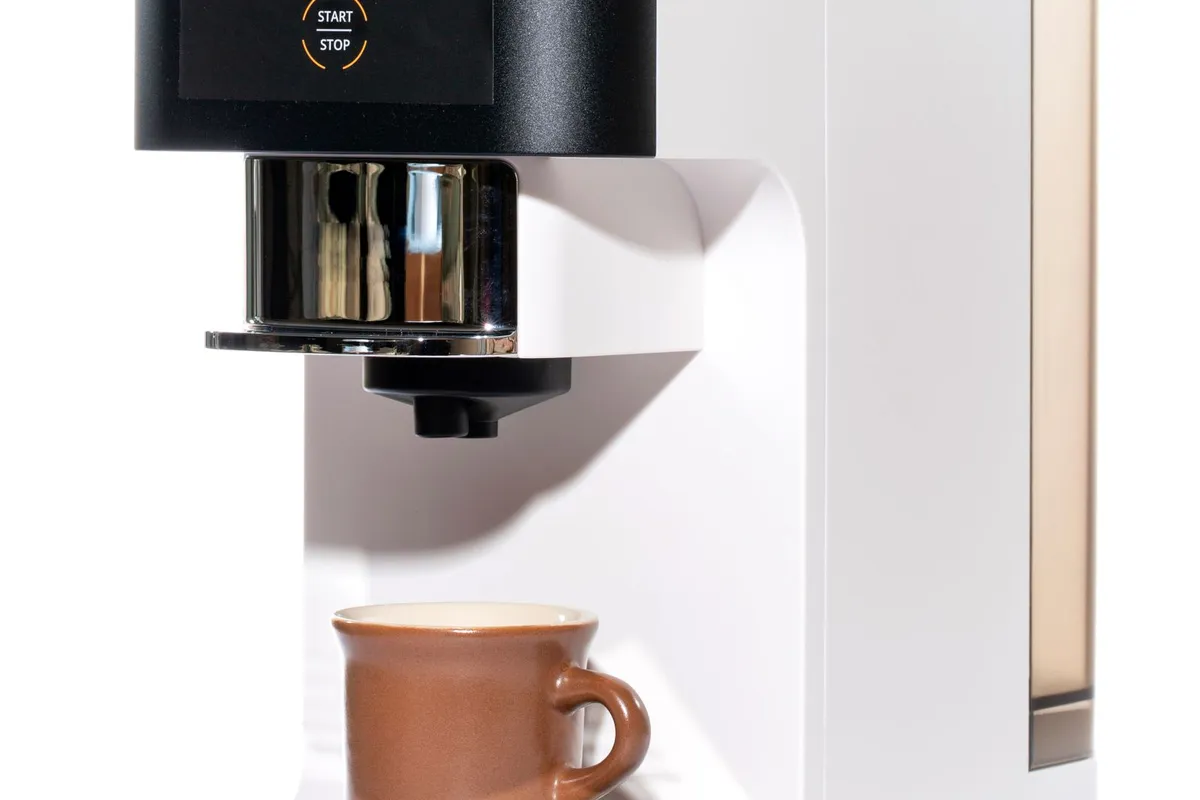 Witte volautomatische koffiemachine met uitloop boven een kopje koffie