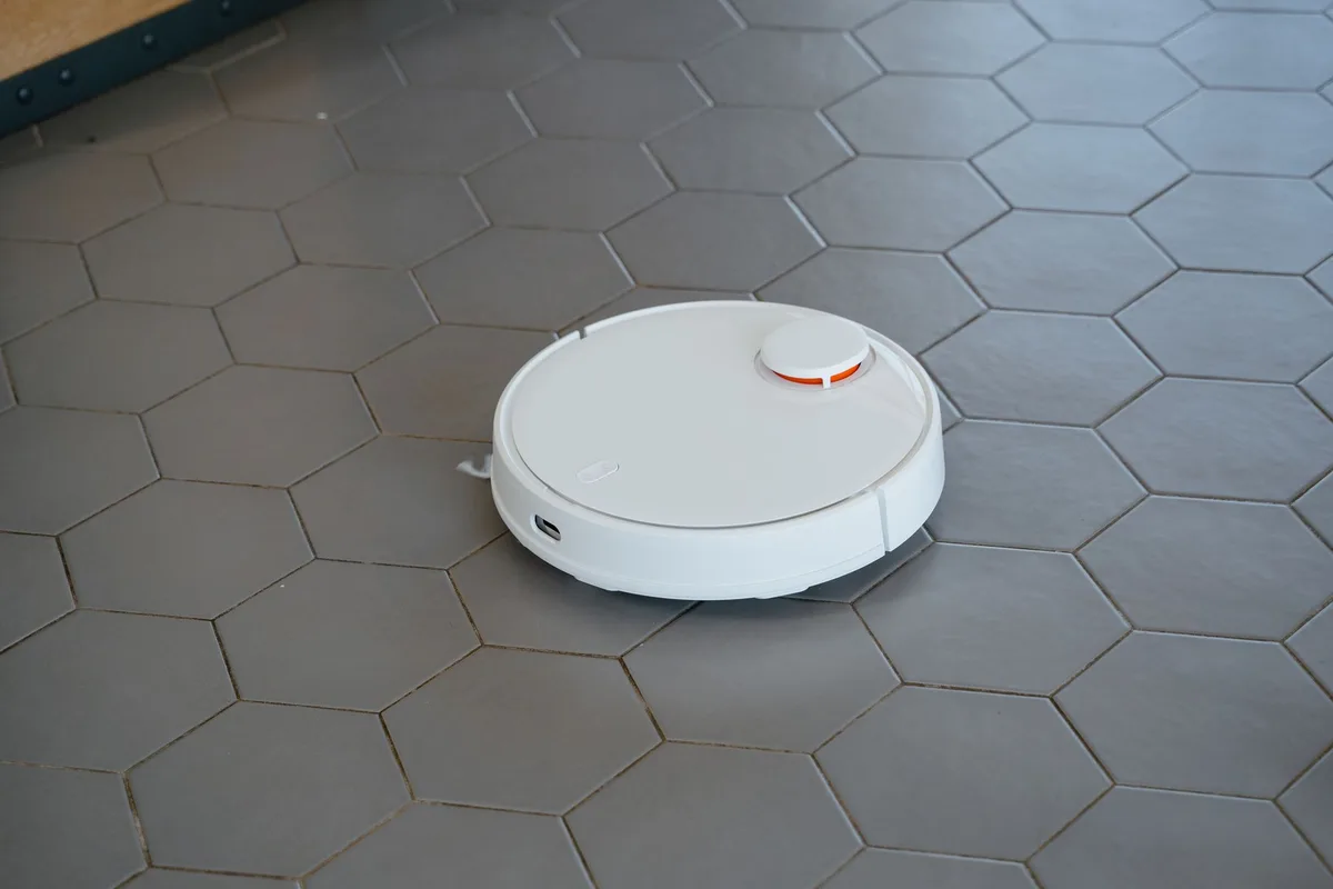 Witte robotstofzuiger rijdt over een grijze vloer met zeshoekige tegels